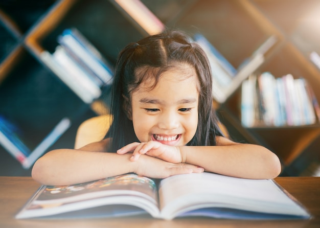 Smiling asian little girl reading book in the living room at home.