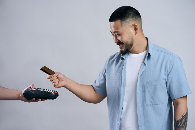 Foto uomo asiatico sorridente che tiene la carta di credito effettuando il pagamento utilizzando la macchina della carta di credito