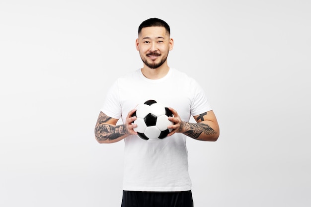 白い背景で隔離のサッカー ボールを保持している笑顔のアジア人男性サッカーをしているハンサムな男性