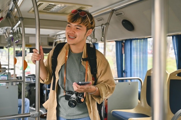 Smiling Asian man with backpack standing in bus and traveling with public transport