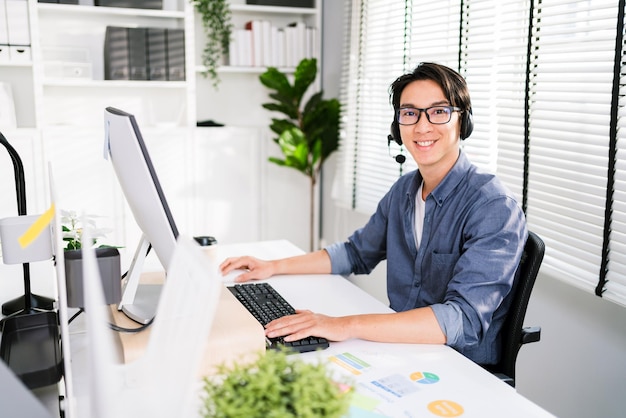 A smiling Asian man working as customer support operator with a headset in a call center