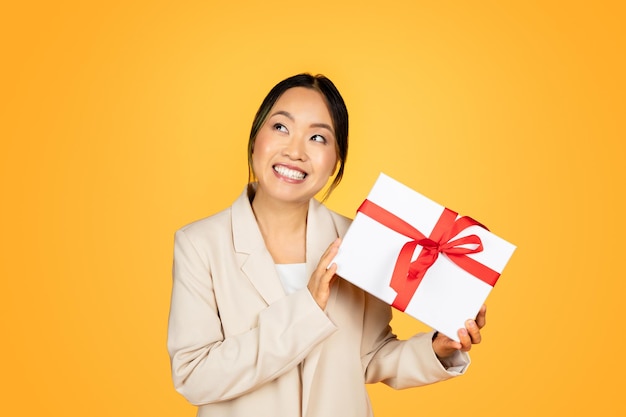 Smiling asian millennial woman joyfully holding a wrapped holiday gift festive atmosphere around
