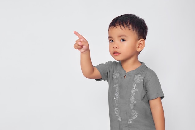 Улыбающийся азиатский мусульманский мальчик, указывающий пальцем на пространство для копирования, изолированное на белом фоне студии