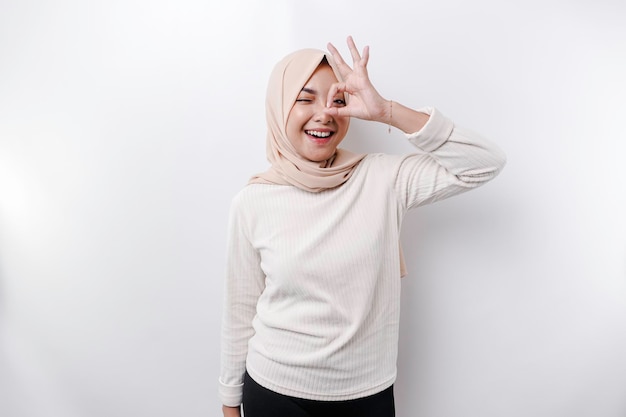 白い背景に分離された OK の手ジェスチャーを与える笑顔のアジアのイスラム教徒の女性