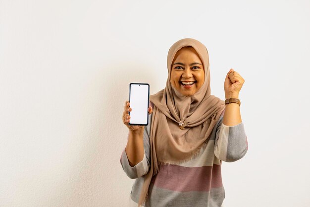 사진 히자브를 입은 미소 짓는 아시아 무슬림 여성이  ⁇ 색 또는 빈 화면의 스마트폰을 들고 있다