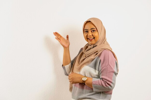 Фото Улыбающаяся азиатская мусульманка в хиджабе представляет что-то на правой стороне рукой