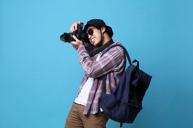 Улыбающийся азиатский фотограф делает снимки с помощью цифровой зеркальной камеры.