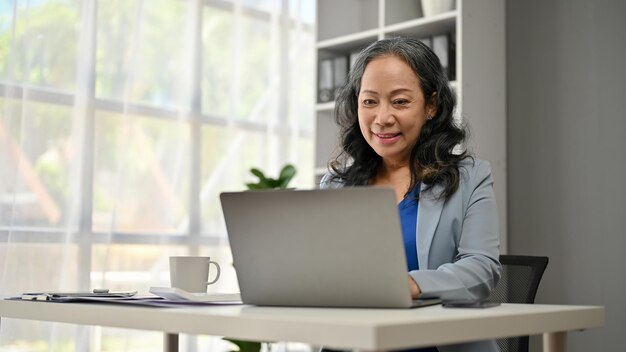 Photo a smiling asian senior businesswoman working on her business work on her laptop