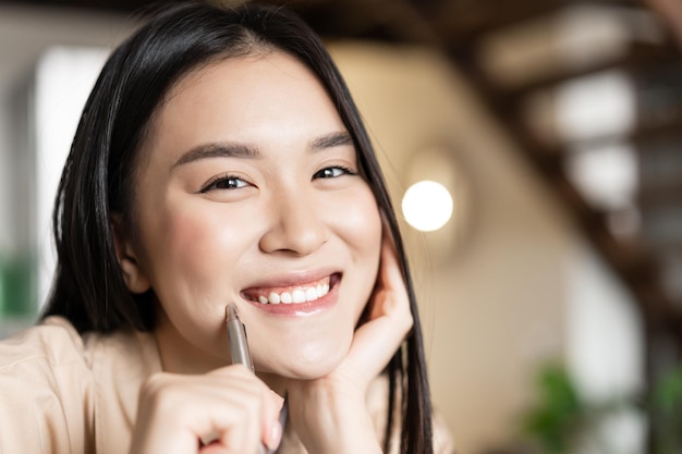 Smiling asian student holding pen looking happy at camera doing homework