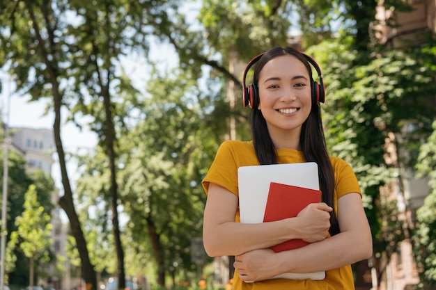 Sorridente studente asiatico che indossa le cuffie che cammina all'università per tornare a scuola concept school