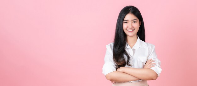 Smiling Asian teenager stand and crossed arms on pink.