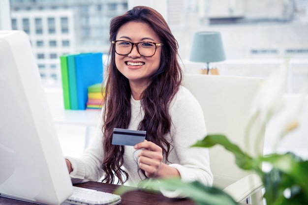 Smiling Asian woman on computer holding credit card in office