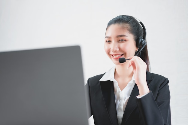 Smiling Asian woman consultant wearing microphone headset of customer support phone operator at workplace.