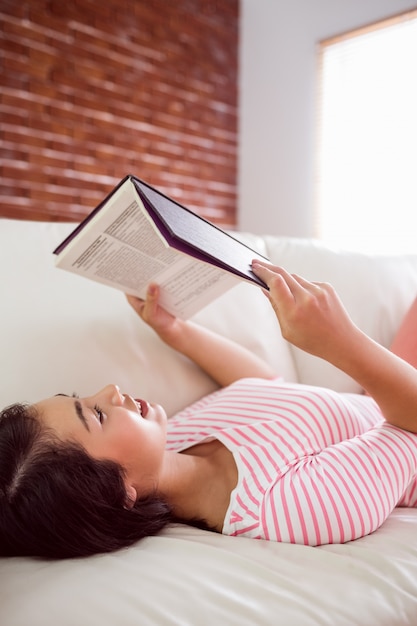 Smiling asian woman on couch reading at home in the living room