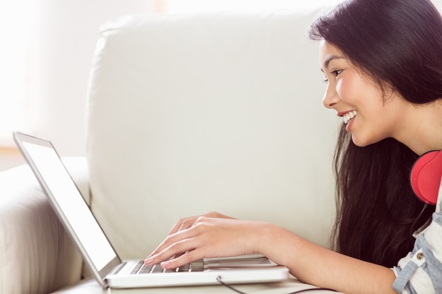 Photo smiling asian woman on couch using laptop