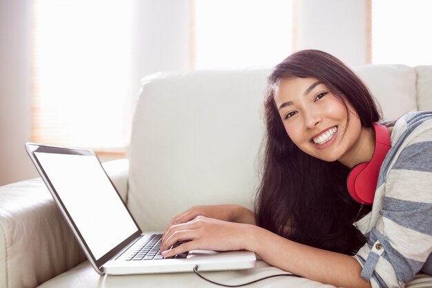 Smiling asian woman on couch using laptop