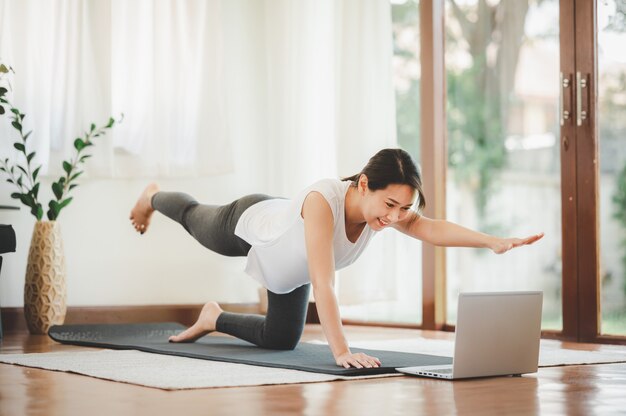 Smiling Asian woman doing one arm one leg plank to exercise core muscle online workout class