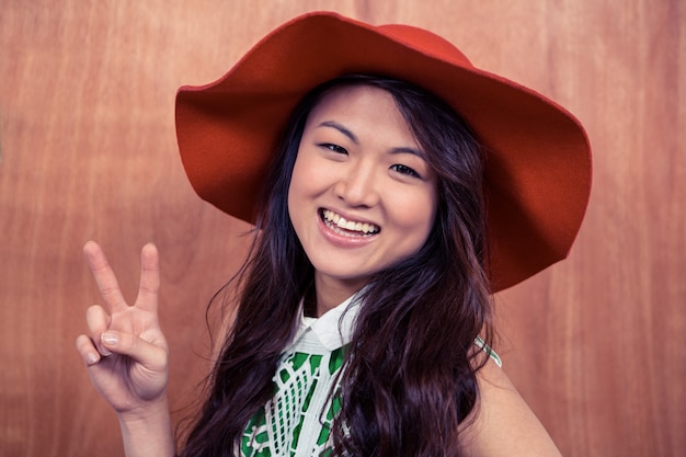 Smiling Asian woman doing peace sign with hand against wooden wall