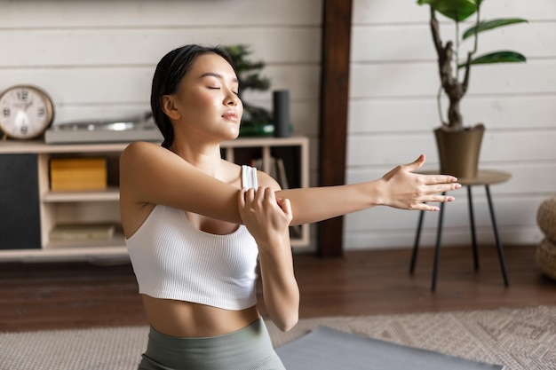 Smiling asian woman doing stretches fitness workout at home in living room wearing sport clothing