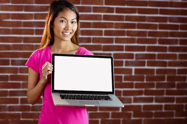 Smiling asian woman holding computer on brick wall