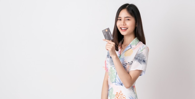 Smiling Asian woman holding credit card and looking forward on white wall with copy space.