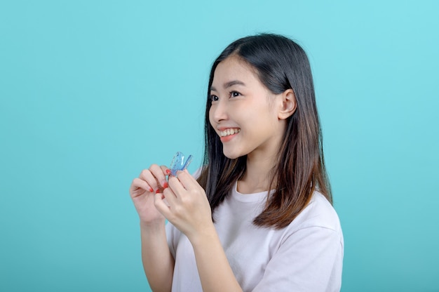 Smiling Asian woman holding orthodontic retainer on blue screen background. Dental care and healthy teeth.