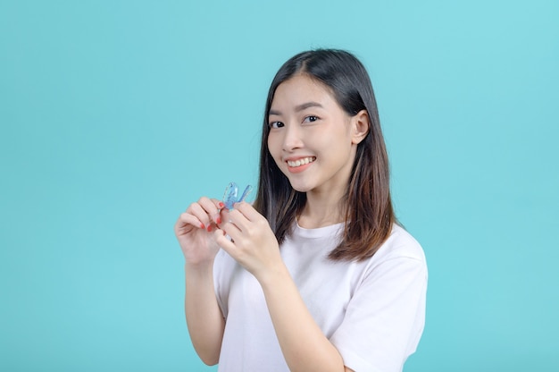 Smiling Asian woman holding orthodontic retainer on blue screen background. Dental care and healthy teeth.