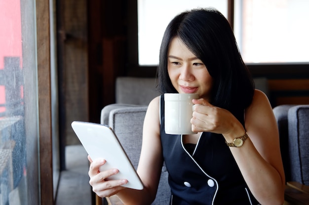 웃는 아시아 여자 커피 한 잔 마시고 디지털 태블릿을 들고.