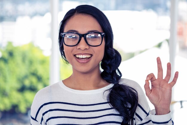 Smiling Asian woman making ok sign with hand in office