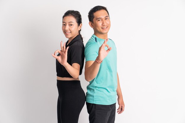 Photo smiling asian woman and man standing back to back with okay gesture on isolated background