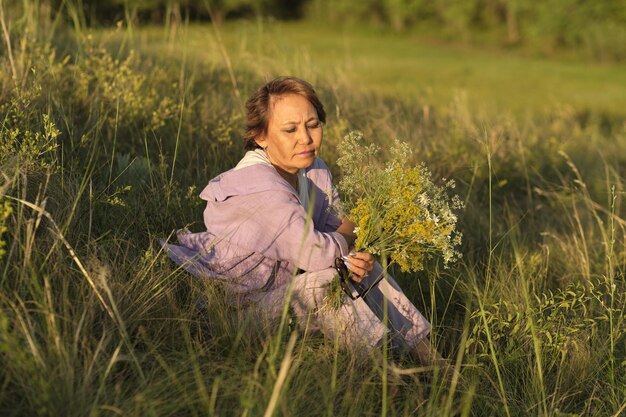 夏の公園で野生の花を持った笑顔の年配のアジア人女性が、ビデオで伝えているのは、