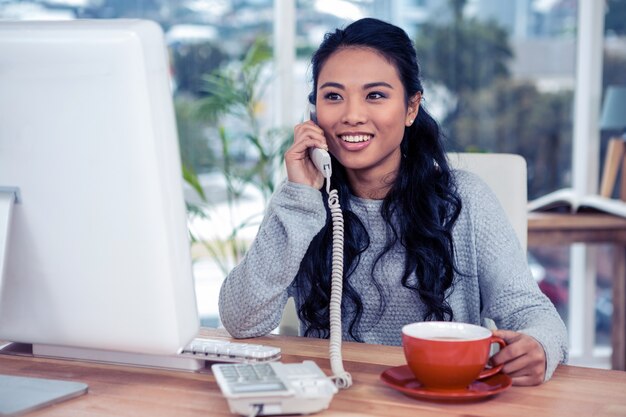 Smiling Asian woman on phone call holding mug in office