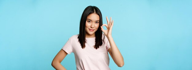 Smiling asian woman showing okay sign gives approval recommends smth good standing over blue person