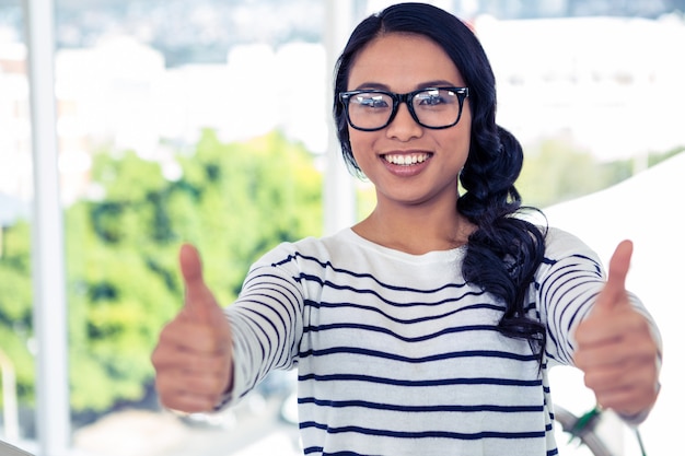 Smiling Asian woman showing thumbs up in office