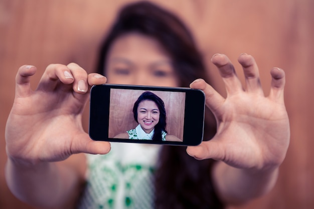 Smiling Asian woman taking selfie against wooden wall