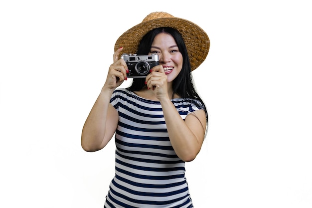 Smiling asian woman tourist in straw hat is taking a photo a vintage photo camera isolated on white