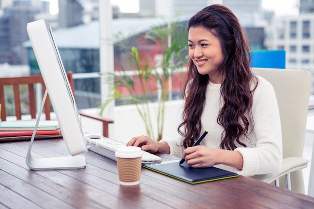 デジタルボードとオフィスでコンピューターを使用して笑顔のアジア女性