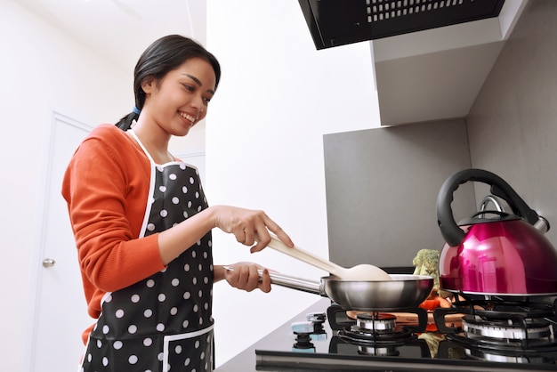 Усмехаясь азиатская женщина используя сковороду и варить