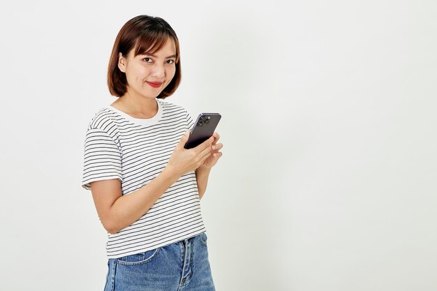 Photo smiling asian woman using a smartphone standing against texting on a mobile phone