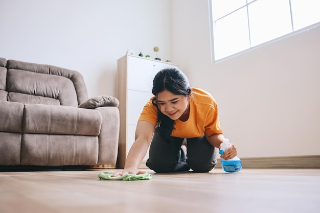 Smiling Asian woman washes the floor with rag and spray bottle at home
