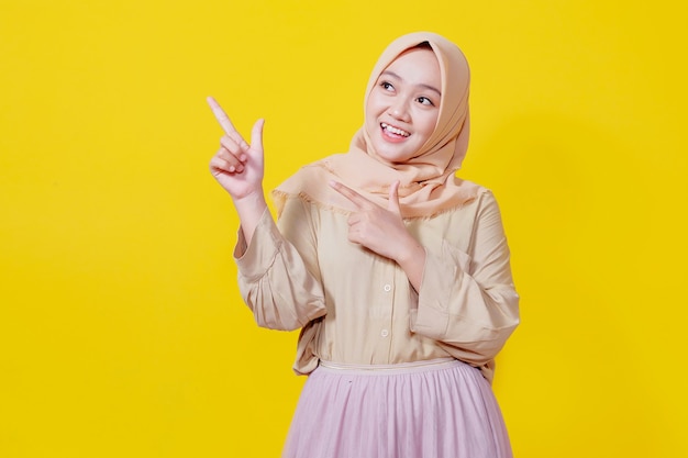 Photo smiling asian woman wearing hijab with her finger pointing isolated on light yellow banner background