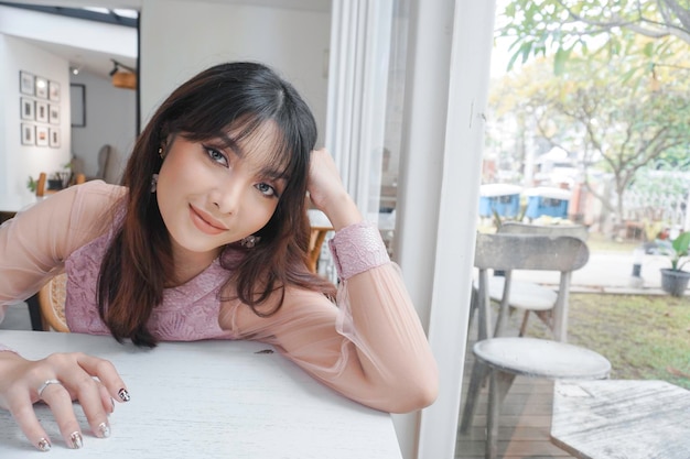 A smiling Asian woman wearing pink dress while sitting near window