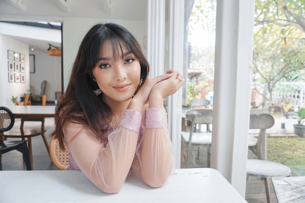 A smiling Asian woman wearing pink dress while sitting near window