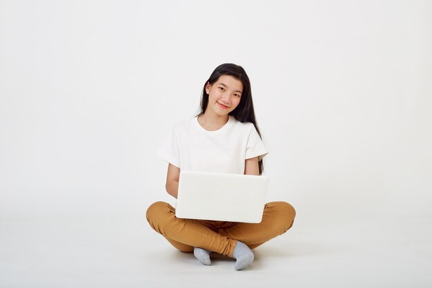 Smiling Asian woman working on laptop computer while sitting on the floor with legs crossed isolated over white âbackground, Back to school concept