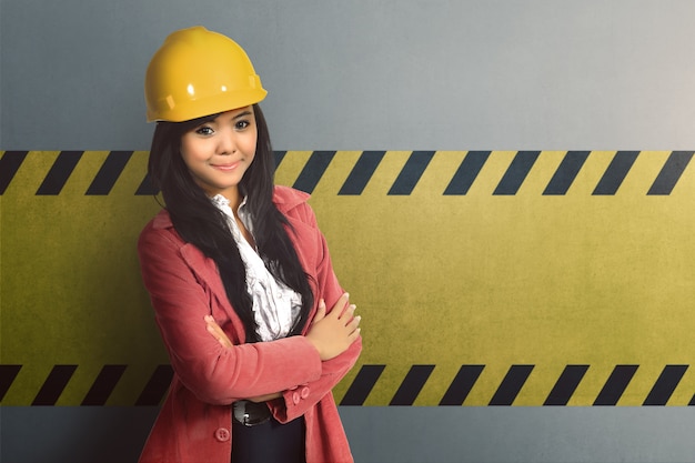 Photo smiling asian worker woman with yellow helmet and crossed hand