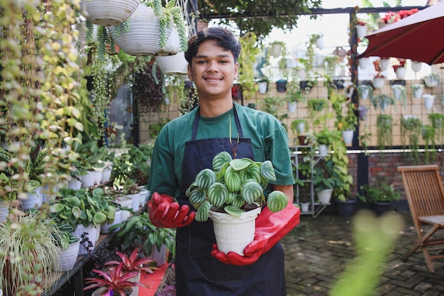 鉢植えの植物を示す笑顔のアジアの若い男性庭師中小企業起業家のコンセプト