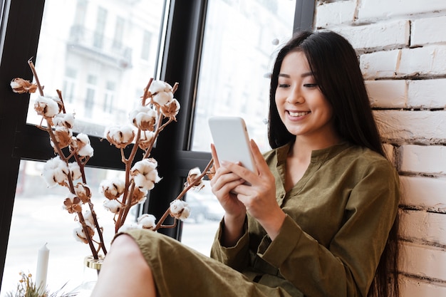 Photo smiling asian young woman chatting by her mobile phone