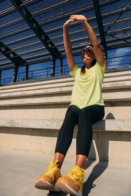 Smiling athletic woman hiding face from sun at stadium