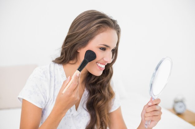 Smiling attractive brunette using a brush and a mirror