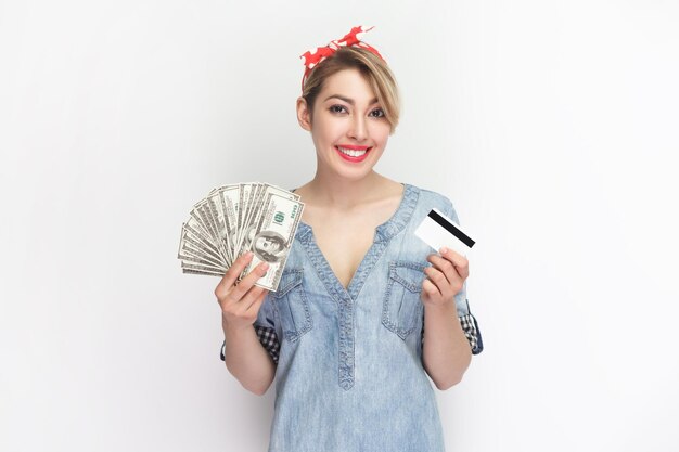 신용카드와 달러 지폐를 들고 서 있는 웃고 있는 매력적인 쾌활한 여성